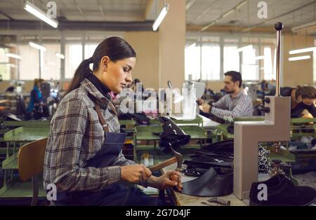 Portrait of young woman shoemaker working at workplace in shoe factory side view Stock Photo