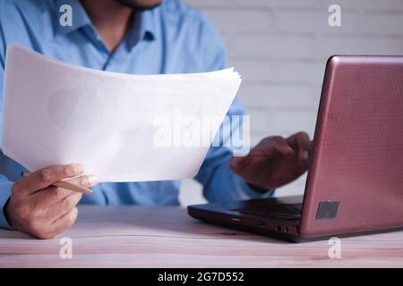 man hand with pen analyzing chart on paper while working on laptop  Stock Photo