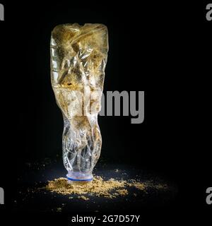 Thrown away plastic bottle with sand from the beach shown like an art sculpture against a black background, waste concept for the abundance and throwa Stock Photo