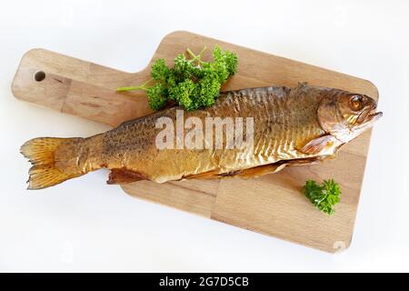 Smoked trout with parsley on a wooden kitchen board and a white background, delicious and healthy fish meal with saturated omega-3 fatty acids, copy s Stock Photo