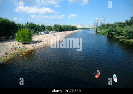 View of the Dnipro river, crowd of people sunbathing on the sandy beach and swimming in the water. Hydropark, Kyiv, Ukraine. Stock Photo