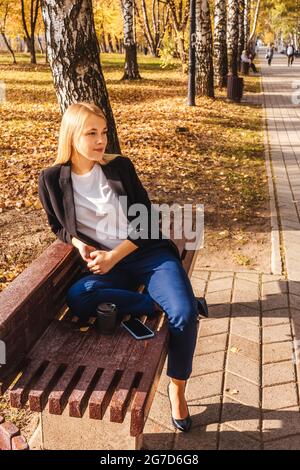 Woman sitting on bench in autumn park, sunny day. Stock Photo