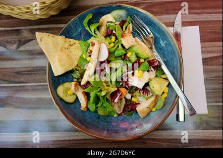 mixed salad with chicken strips and bread in a blue plate as a healthy summer meal, high angle view from above, selected focus Stock Photo
