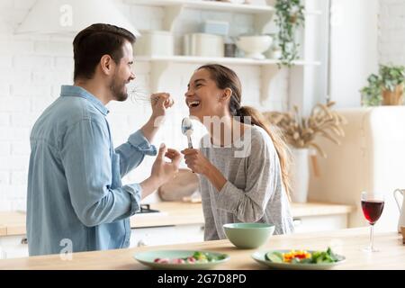 Cheery couple holding kitchenware singing having fun together in kitchen Stock Photo