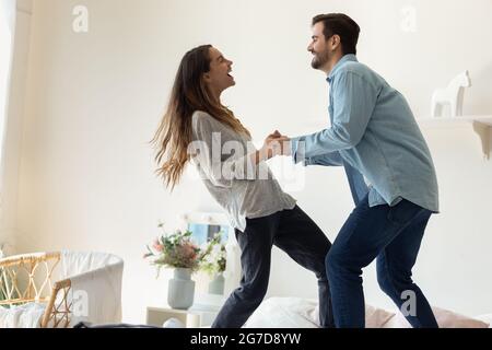 Happy couple holding hands standing on bed in cozy bedroom Stock Photo