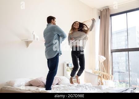 Funny couple dance jumping on bed in modern bedroom Stock Photo