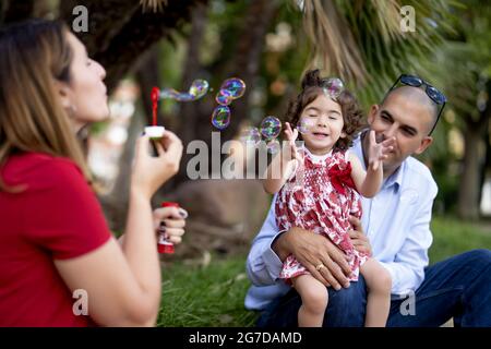Mother blowing some soap bubbles while having a nice family time with her husband and daughter Stock Photo