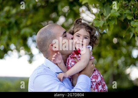 Father hugging and kissing her little daughter while walking in a park Stock Photo