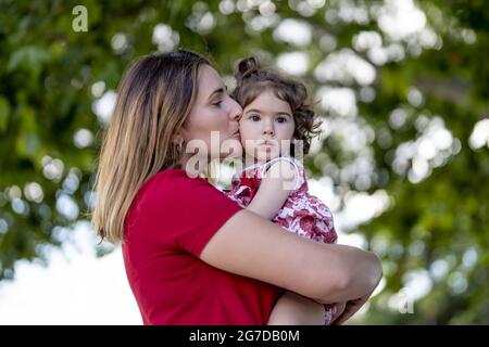 Mother hugging and kissing her little daughter while walking in a park Stock Photo