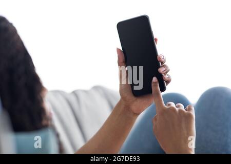 Mockup, blank screen of cell phone. Woman hand texting, using mobile on sofa at home Stock Photo