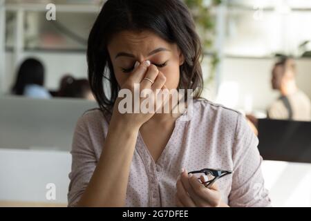 Tired mixed race Black business woman touching, rubbing nose bridge