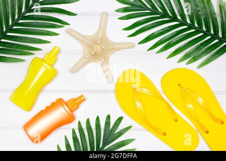 Summer sea beach vacation creative concept. Sunscreen spray, flip flop sandals, starfish with tropical palm leaves on white wooden boards. Top view Stock Photo