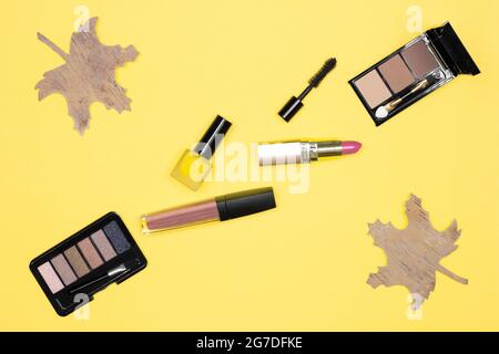 Autumn makeup flat lay. Make-up products brown, bronze, golden colors with fall decorations on yellow background. Top view Stock Photo