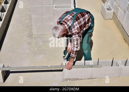 The mason on the construction site measures the perpendicularity of the walls with a spirit level Stock Photo