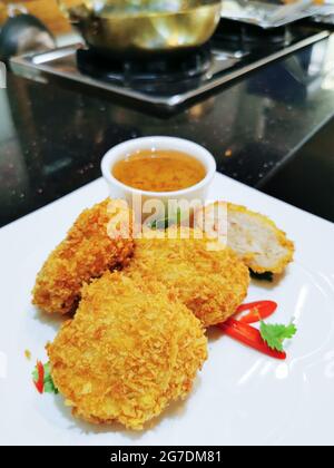 Deep fried prawn cake served on white ceramic plate with sweet and sour dipping sauce on small bowl on the plate, garnish with sliced red chili pepper Stock Photo