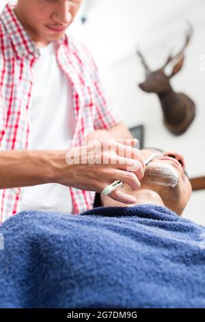 Young man getting an old-fashioned shave with straight razor Stock Photo