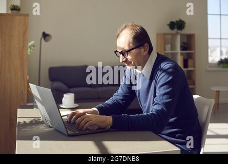Side view on mature man in eyewear working on laptop remotely at home office Stock Photo