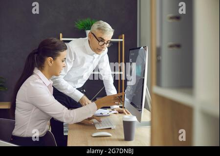 Two business colleagues looking at the screen of their office computer and talking Stock Photo