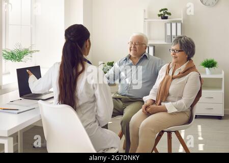 Happy mature couple and their doctor communicating while using laptop during medical appointment. Stock Photo