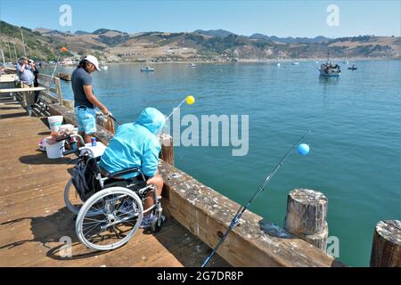 woman in wheelchair fishing on public pier in Port San Luis, Avila, California, with hoodie Hoody, on sunny day at the beach with family Stock Photo