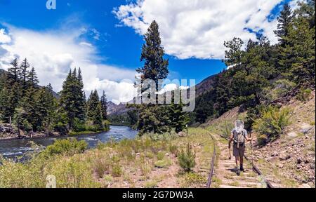 Landscape image of a fly-fisher walking on rail raod track along Rio Grande river in Colorado Stock Photo