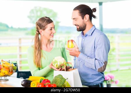 Man and woman unpacking fruits and vegetables out of grocery shopping bag in home kitchen Stock Photo