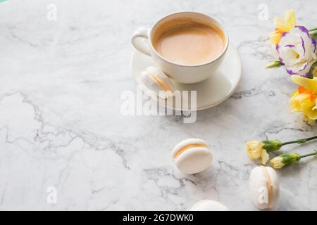 White cup of black coffee, served on white saucer with macaroons biscuits and magnolia flower blossom branch over gray texture background. Flat lay, s Stock Photo