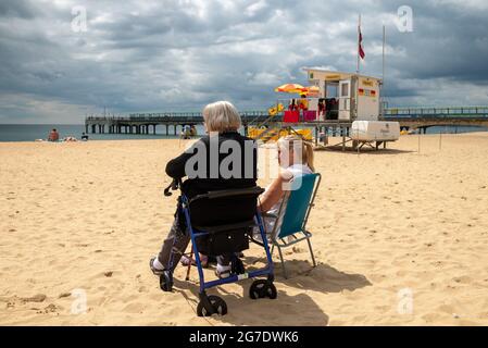 Boscombe, Bournemouth, Dorset, UK, 13th July 2021, UK Weather: Cloudy with sunny spells and warm in the afternoon on the south coast as summer begins to make a return. People relax on the beach near the pier at the start of what is expected to become a long dry and possibly hot spell of weather. Credit: Paul Biggins/Alamy Live News Stock Photo