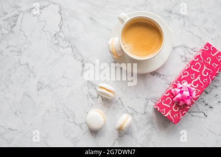 White cup of black coffee, served on white saucer with macaroons biscuits and magnolia flower blossom branch over gray texture background. Flat lay, s Stock Photo