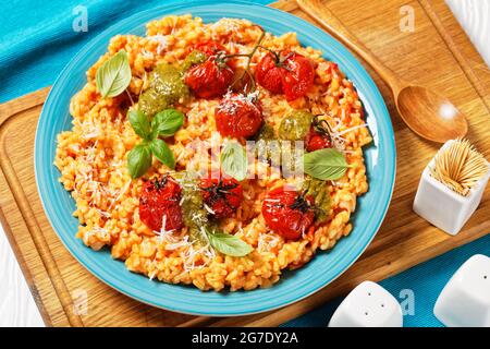 close-up of creamy tomato risotto with cherry tomatoes and sauce pesto on a blue plate on a cutting board Stock Photo