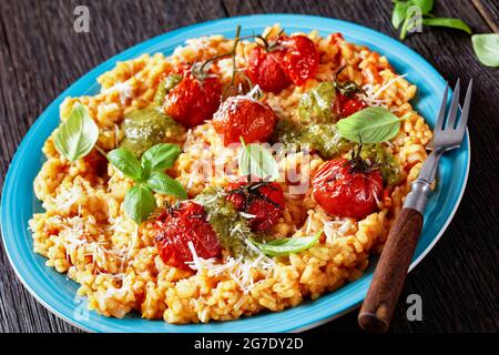 creamy tomato risotto with cherry tomatoes and sauce pesto on a blue plate, italian cuisine, close-up Stock Photo