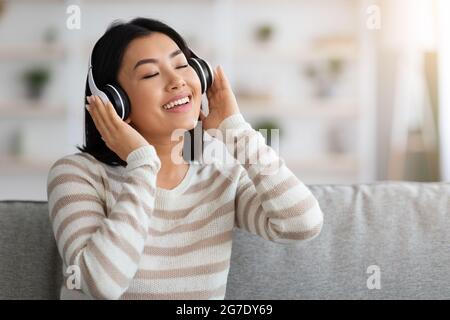 Portrait Of Relaxed Asian Woman In Headphones Listening Music With Closed Eyes Stock Photo