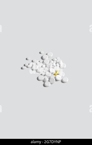 One yellow pill surrounded by white pills on gray background. The concept of medical treatment Stock Photo