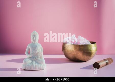 Decorative white Buddha statuette and tibetian singing bowl on pink background. Meditation and relaxation ritual. Exotic massage. Minimalism. Direct Stock Photo