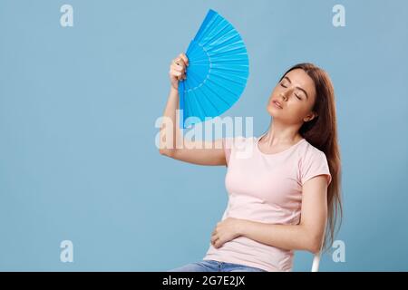 Overheated young lady sitting on chair with paper fan Stock Photo