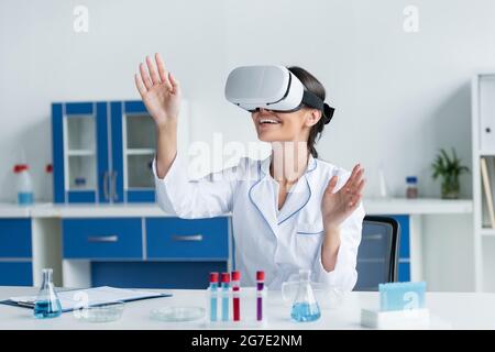 Smiling scientist using virtual reality headset near clipboard and test tubes Stock Photo