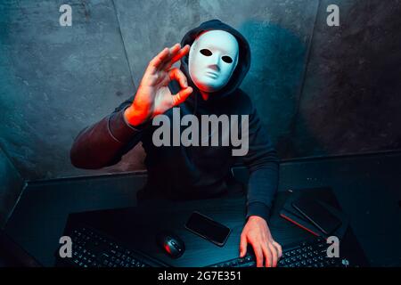 Anonymous hacker wearing face mask working on computer in dark room Stock Photo