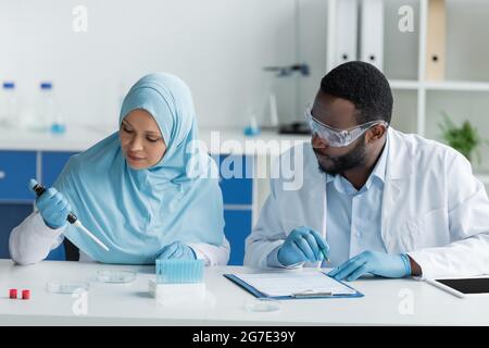 African american and arabian scientists working with petri dishes, digital tablet and clipboard in lab Stock Photo
