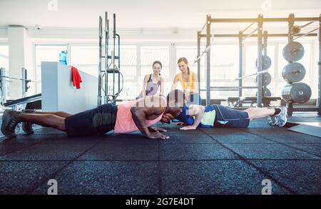 Two men have a push-up competition in the gym with girls cheering them up Stock Photo