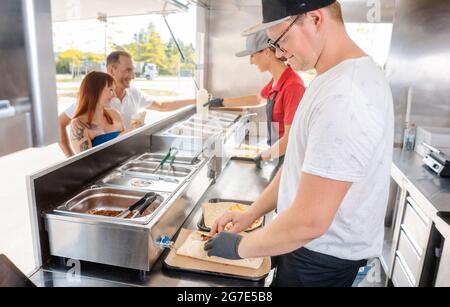 Young chefs in a food truck preparing Mexican food for their waiting customers Stock Photo