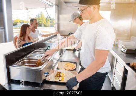 Young chefs in a food truck preparing Mexican food for their waiting customers Stock Photo