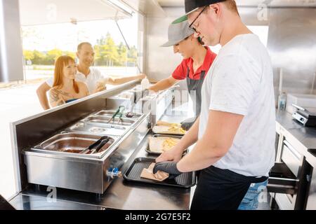 Young chefs in a food truck preparing Mexican food for their waiting customers Stock Photo