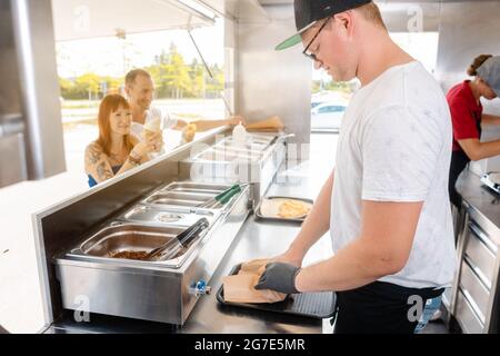 Young chefs in a food truck preparing Mexican food for their waiting customers Stock Photo