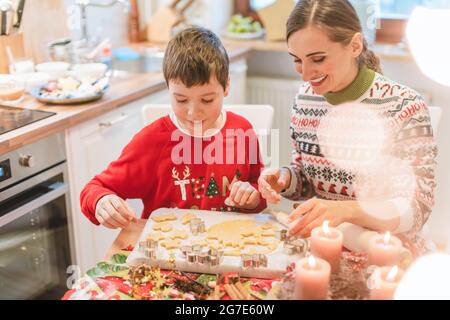 Mother and son decorating Christmas cookies on the sheet in the family kitchen Stock Photo