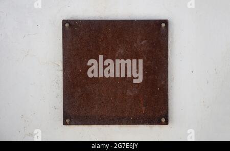 Sign plate rusty metal, brown color, mounted with screws on white wall. Blank label mockup, Business signage template, copy space Stock Photo