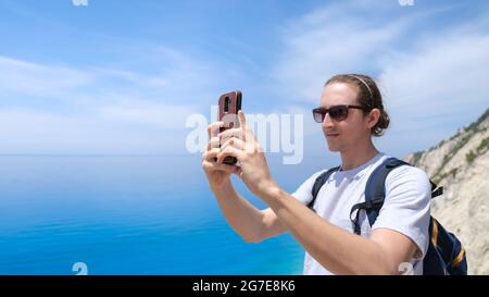 Young man taking pictures of beautiful beach with smartphone Stock Photo