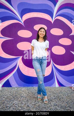 Young Asian Woman in 1960s Apparel Standing in Front of 1960s Style Mural Stock Photo