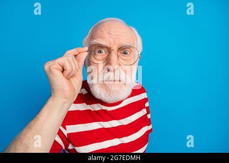 Close-up portrait of attractive discontent grey-haired man touching specs looking at you isolated over bright blue color background Stock Photo