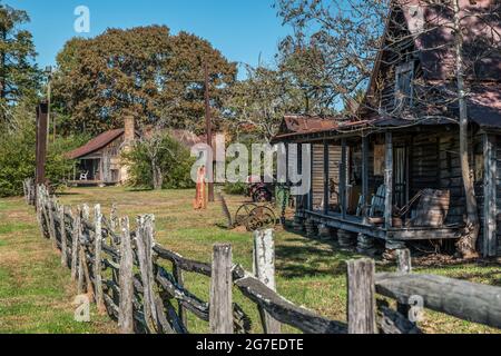 Side view of an old homestead abandoned with farm equipment truck and gas pump left outdoors to rust away surrounded by a weathered rustic fence on a Stock Photo