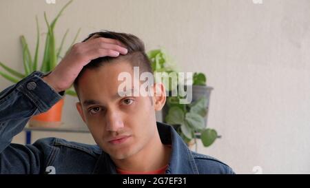 Young depressed Indian male holding his head in his hand with houseplants in the background Stock Photo